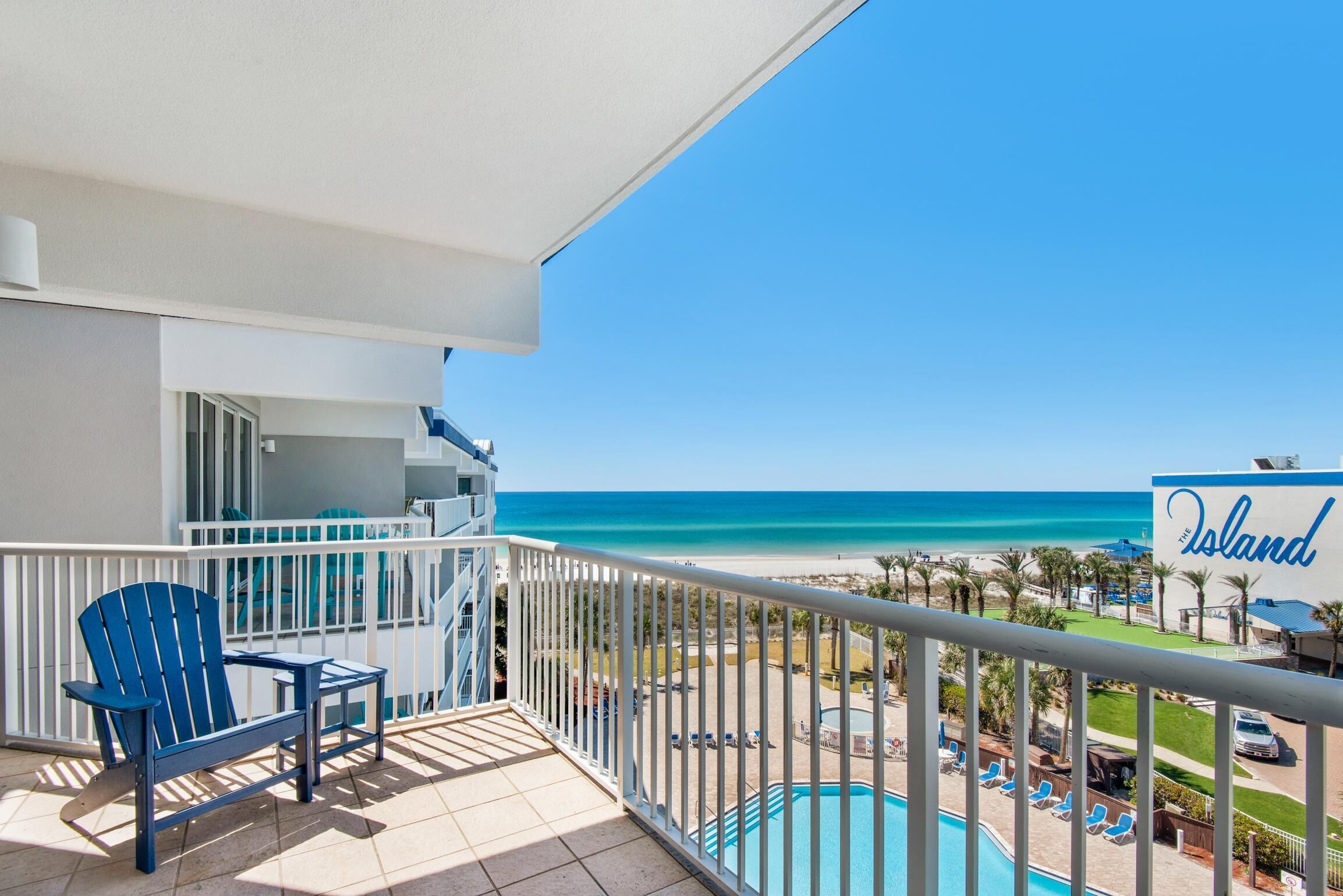 A balcony with a view of the beach, a pool, and a sign that reads "The Island".