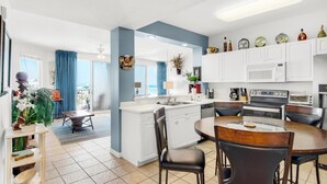 A modern kitchen with white cabinets, a central island, and a dining area with a round table and chairs. - Destin West Gulfside #608 (Fort Walton Beach)