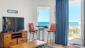 A room with a TV, wooden furniture, two bar stools, a small table, a balcony with a view of the sea, and a 'Welcome' sign. - Destin West Gulfside #608 (Fort Walton Beach)