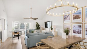 A spacious living room with a wooden dining table, a blue sofa, and a ceiling fan. - Chateau La Mer II #103- Dreamland Destin (Destin)