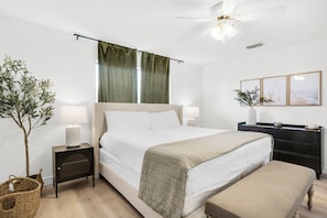 A neatly arranged bedroom with a bed, bedside tables, a nightstand, a bench, a ceiling fan, and a wall-mounted TV.