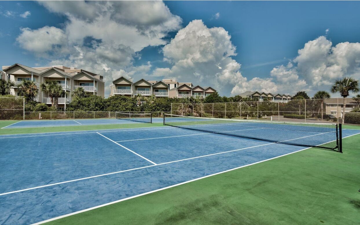 A tennis court with a net, surrounded by a fence and palm trees.