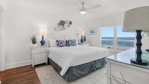A bedroom with a bed, nightstands, a desk, a ceiling fan, and a view of the ocean. - Sea Oats 601 (Fort Walton Beach)