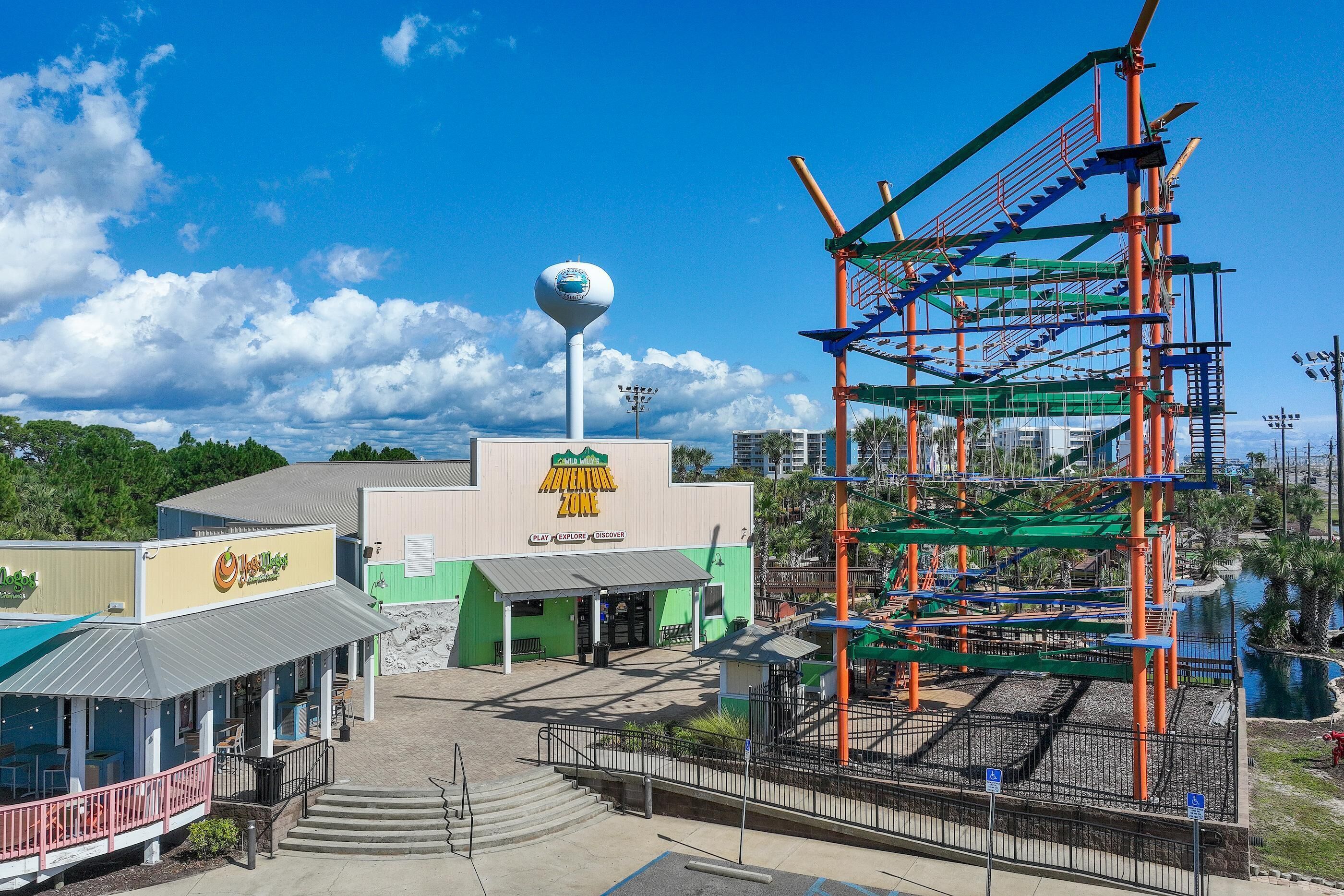 Zona de atracciones al aire libre con una torre de agua, una estructura de juegos y un edificio con un letrero que dice "Adventure Zone".