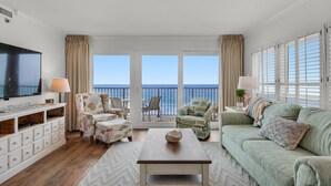 A spacious living room with a large flat-screen TV, comfortable seating, a coffee table, and a view of the ocean through large windows. - Sea Oats 601 (Fort Walton Beach)