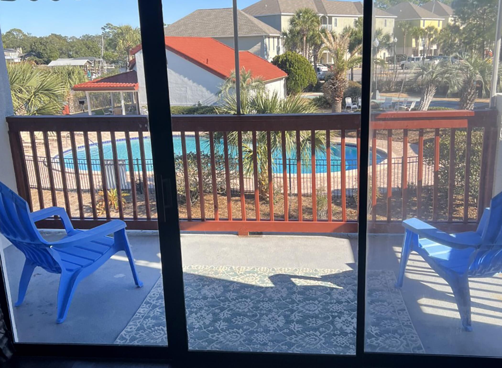 Un balcón con vista a una piscina, dos sillas azules y un tapete estampado.