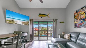 A modern living room with a dining area, a balcony with a view of a swimming pool, and a fish decoration.