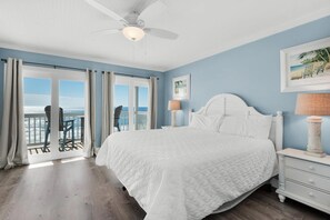 A bedroom with a large bed, a ceiling fan, a nightstand, and a view of the ocean through a sliding door. - Crystal Views (Destin)