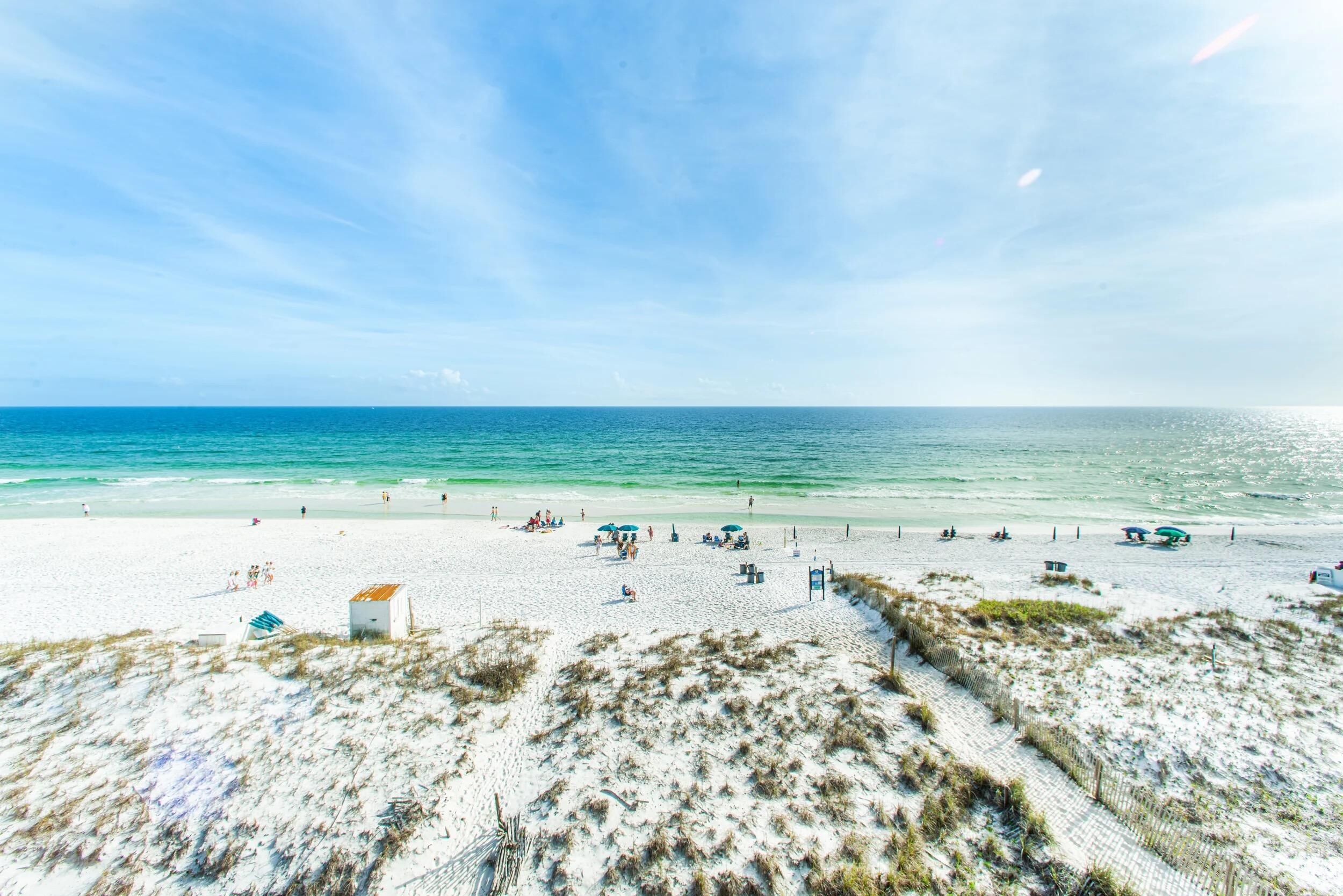 A beach with white sand, a few umbrellas, and a small building.