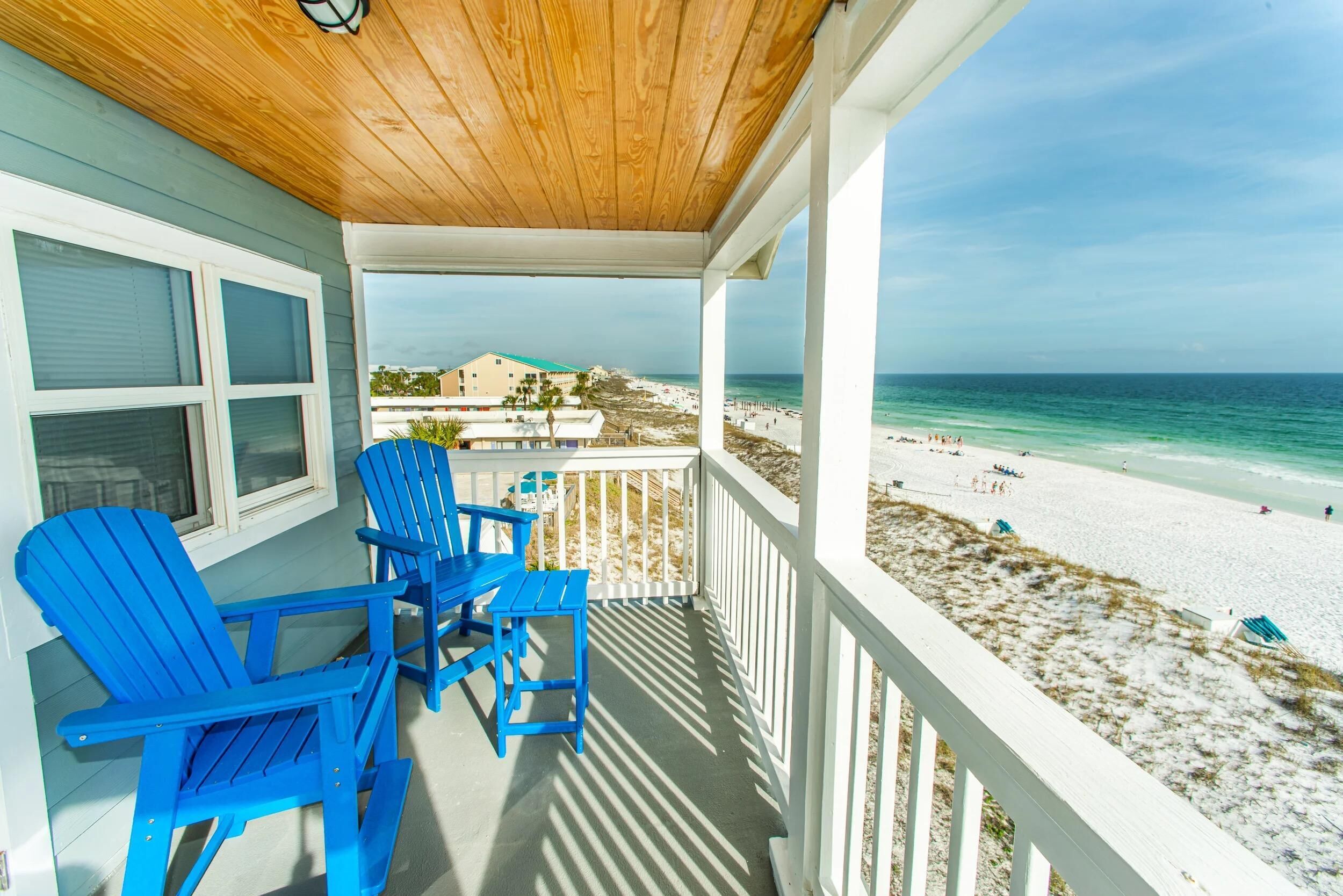 A covered porch with blue Adirondack chairs and a view of the beach.