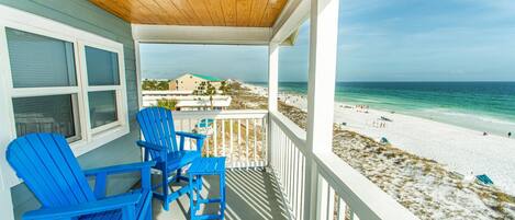 A covered porch with blue Adirondack chairs and a view of the beach.