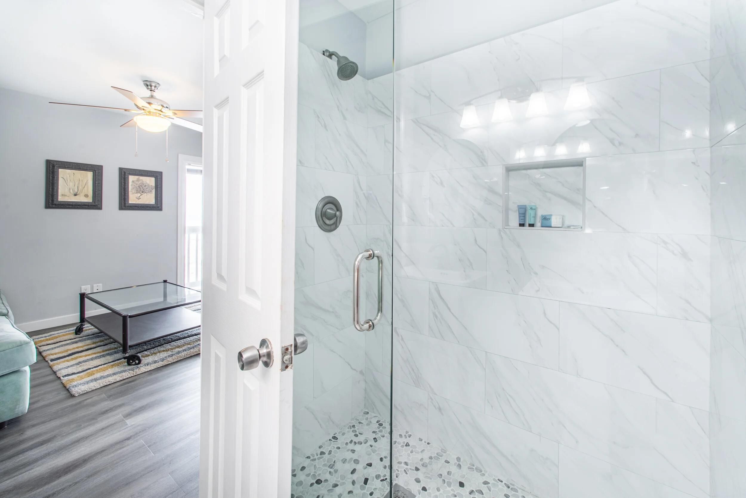 A modern bathroom with a glass shower enclosure, marble tiles, and a small shelf with toiletries.