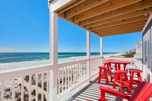 A covered outdoor area with a wooden ceiling, white railings, and red chairs. - Crystal Views (Destin)