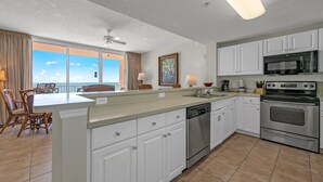 A modern kitchen with white cabinets, stainless steel appliances, and a large island with a dishwasher. - Majestic Beach Towers 1-407 (Panama City Beach)
