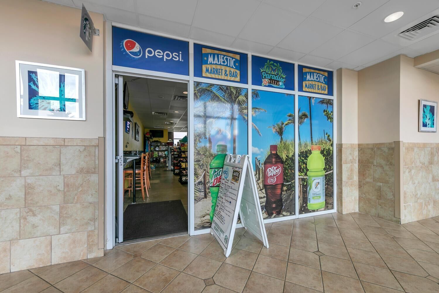 The entrance to a store with a Pepsi sign, a Paradise Pizza sign, and a Majestic Market & Bar sign.