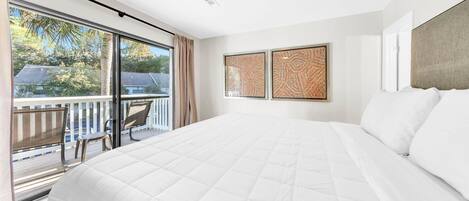 Habitació d'hotel amb un llit gran, un balcó amb una cadira i dos quadres emmarcats a la paret.