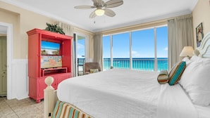 A hotel room with a large bed, a television, a balcony with a view of the ocean, and a ceiling fan. - Boardwalk 508 (Panama City Beach)