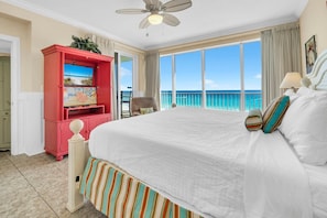A hotel room with a large bed, a television, a balcony with a view of the ocean, and a ceiling fan. - Boardwalk 508 (Panama City Beach)