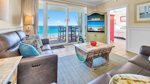 A living room with a sofa, a coffee table, and a TV. There is a balcony with a view of the ocean. - Boardwalk 508 (Panama City Beach)