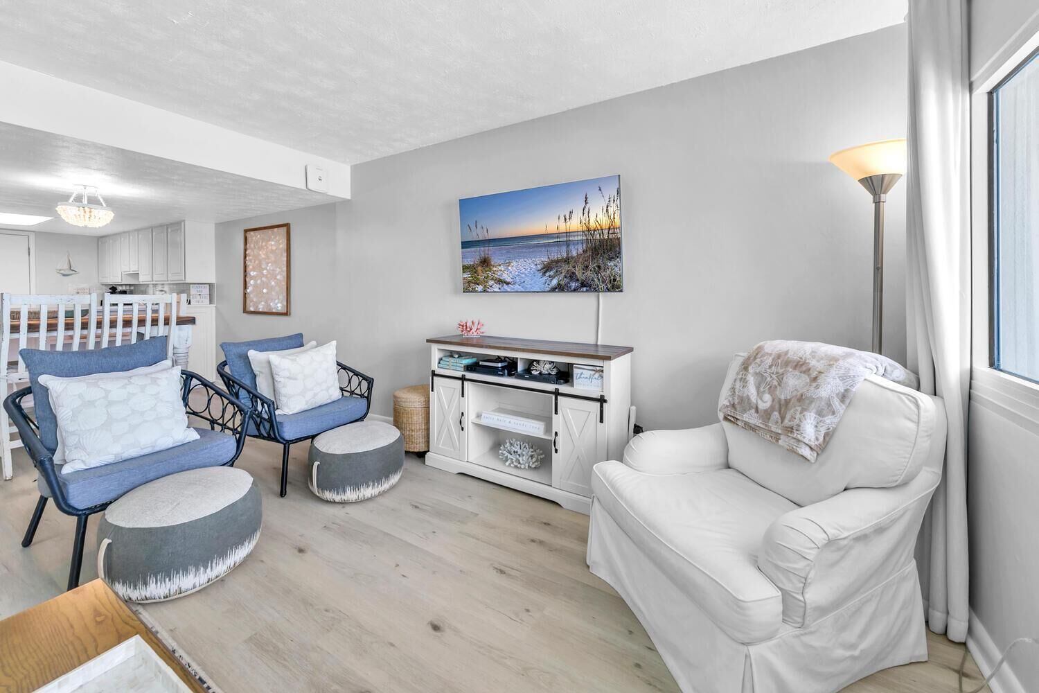 Un salon moderne avec un canapé blanc, des fauteuils bleus et un fauteuil blanc. Un tableau orne le mur, ainsi qu’une lampe et un meuble contenant des objets décoratifs.