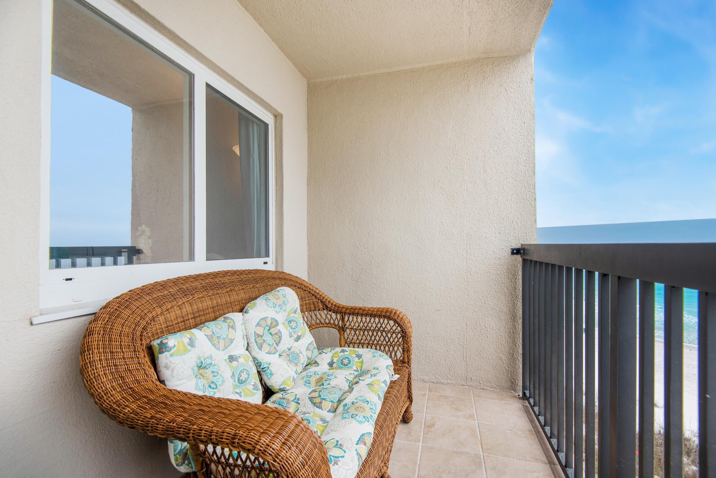 A wicker chair with patterned cushions on a balcony with a view of the ocean.