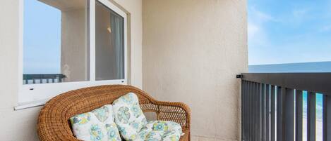 A wicker chair with patterned cushions on a balcony with a view of the ocean.