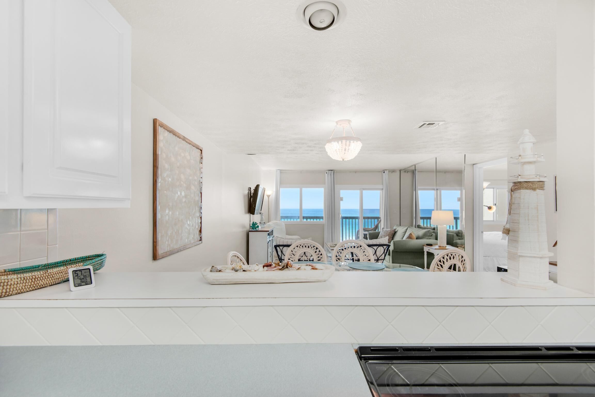 A modern kitchen with a white countertop, a clock, and a view of the ocean through large windows.