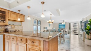 A spacious kitchen with wooden cabinets, a large island, pendant lights, and a view to the dining area. - Mainsail 234 (Miramar Beach)