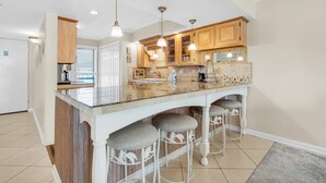 A kitchen with a large island, bar stools, wooden cabinets, and pendant lighting. - Mainsail 234 (Miramar Beach)