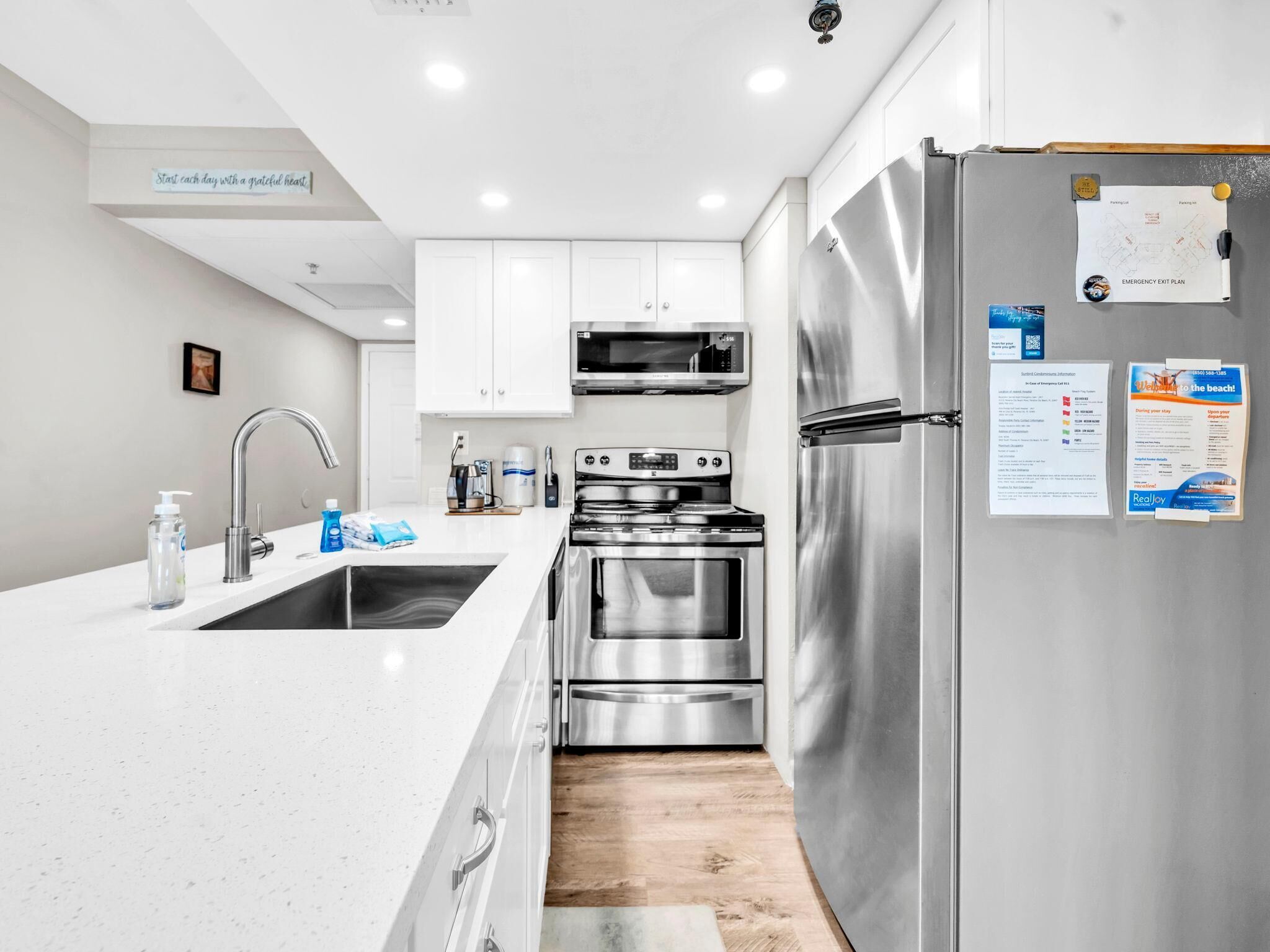 A modern kitchen with white cabinets, stainless steel appliances, and a wooden floor.