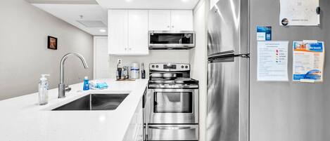 A modern kitchen with white cabinets, stainless steel appliances, and a wooden floor.
