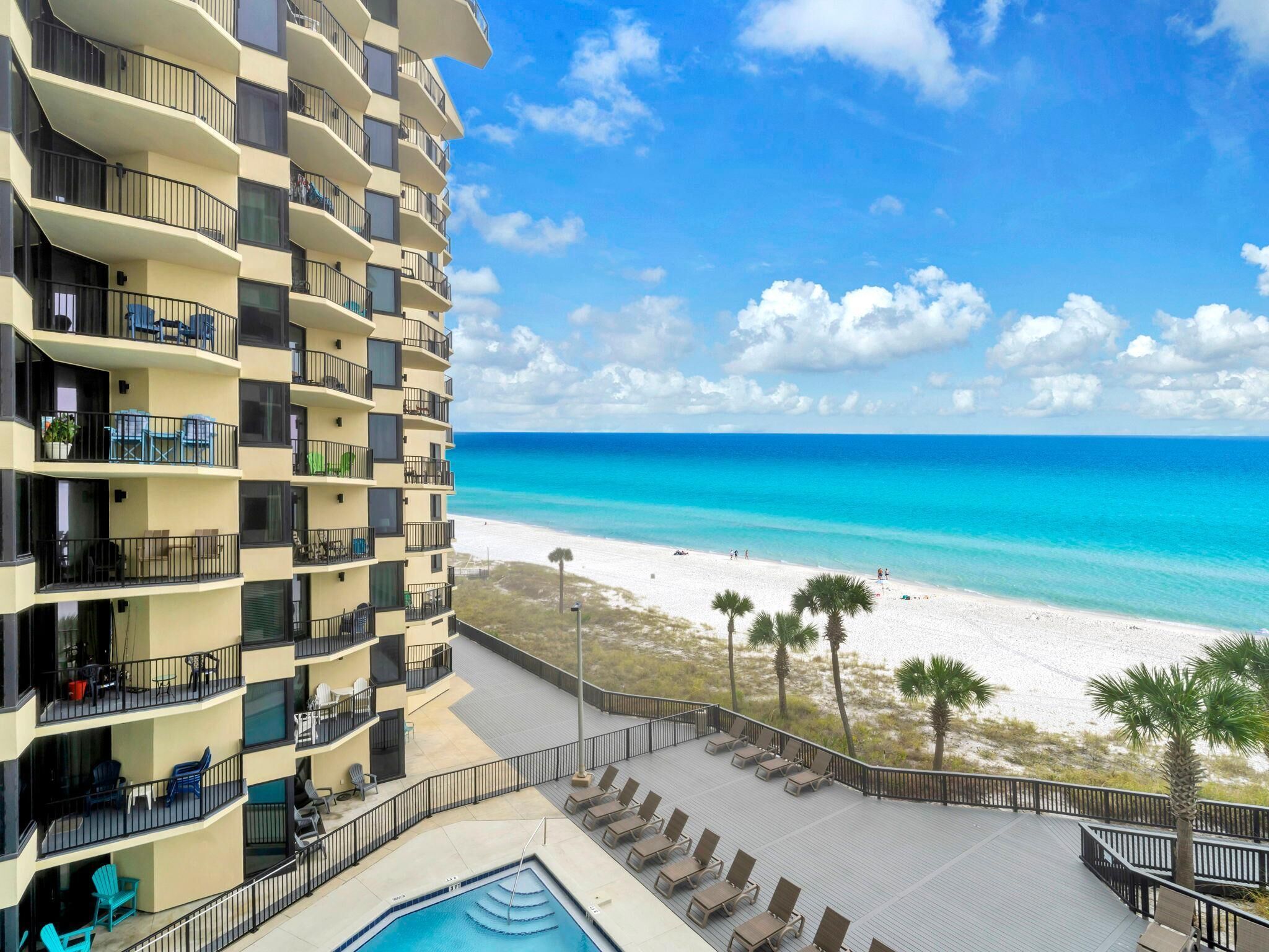 A high-rise hotel with multiple balconies, a pool, and a beach view.