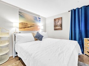 Une chambre à coucher avec un grand lit, une table de chevet, une lampe, un tableau accroché au mur et un rideau bleu.