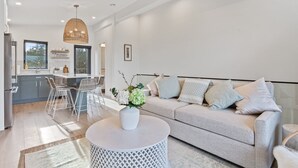 Un salon moderne avec un canapé gris, une table basse ronde et un coin repas comprenant une table et des chaises blanches.