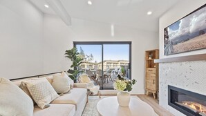Un salon moderne avec un canapé, une cheminée et une vue sur un balcon aménagé avec du mobilier d’extérieur.