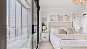 Une chambre moderne avec un grand lit, des tables de chevet, une petite table et une vue sur l’extérieur grâce à une porte-fenêtre coulissante.