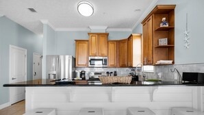Eine moderne Küche mit Holzschränken, einem Edelstahl-Kühlschrank, einer Mikrowelle und einer großen Kochinsel mit Barhocker.