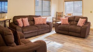 A living room with two brown sofas and patterned throw pillows, a wooden coffee table, and a wooden floor.