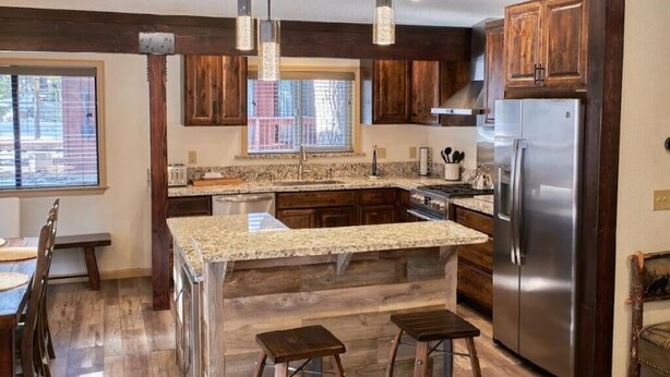 A kitchen with wooden cabinets, granite countertops, a stainless steel refrigerator, and pendant lighting.