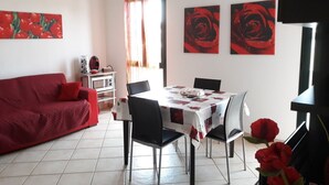 Un coin repas avec une table et des chaises, un canapé rouge et deux tableaux représentant des roses rouges accrochés au mur.