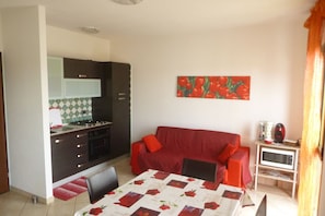 A compact living space with a kitchenette, a red sofa, a dining table, and a microwave. - Large apartment of 65 sqm on the first floor of a building without a lift (stairs to access) perfect for 3 people.The accommodation is located in the center of Pula a few steps from the famous shopping gallery.Nora Beach and Su Gunventeddu are both a 7-m (Cagliari)