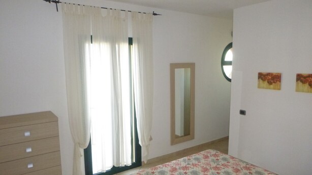 Une chambre à coucher comprenant un lit, une commode, une fenêtre avec des rideaux, un miroir et des œuvres d’art murales.