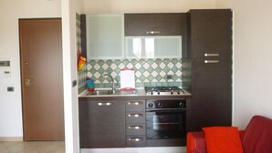 Une cuisine compacte équipée d’une cuisinière à gaz, d’un four et d’un four à micro-ondes. Une porte donne accès à une autre pièce et le mur derrière le plan de travail est recouvert de carreaux.