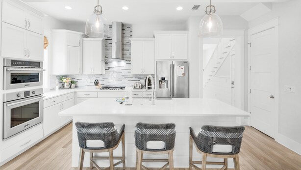 A modern kitchen with white cabinetry, stainless steel appliances, and three wicker bar stools.