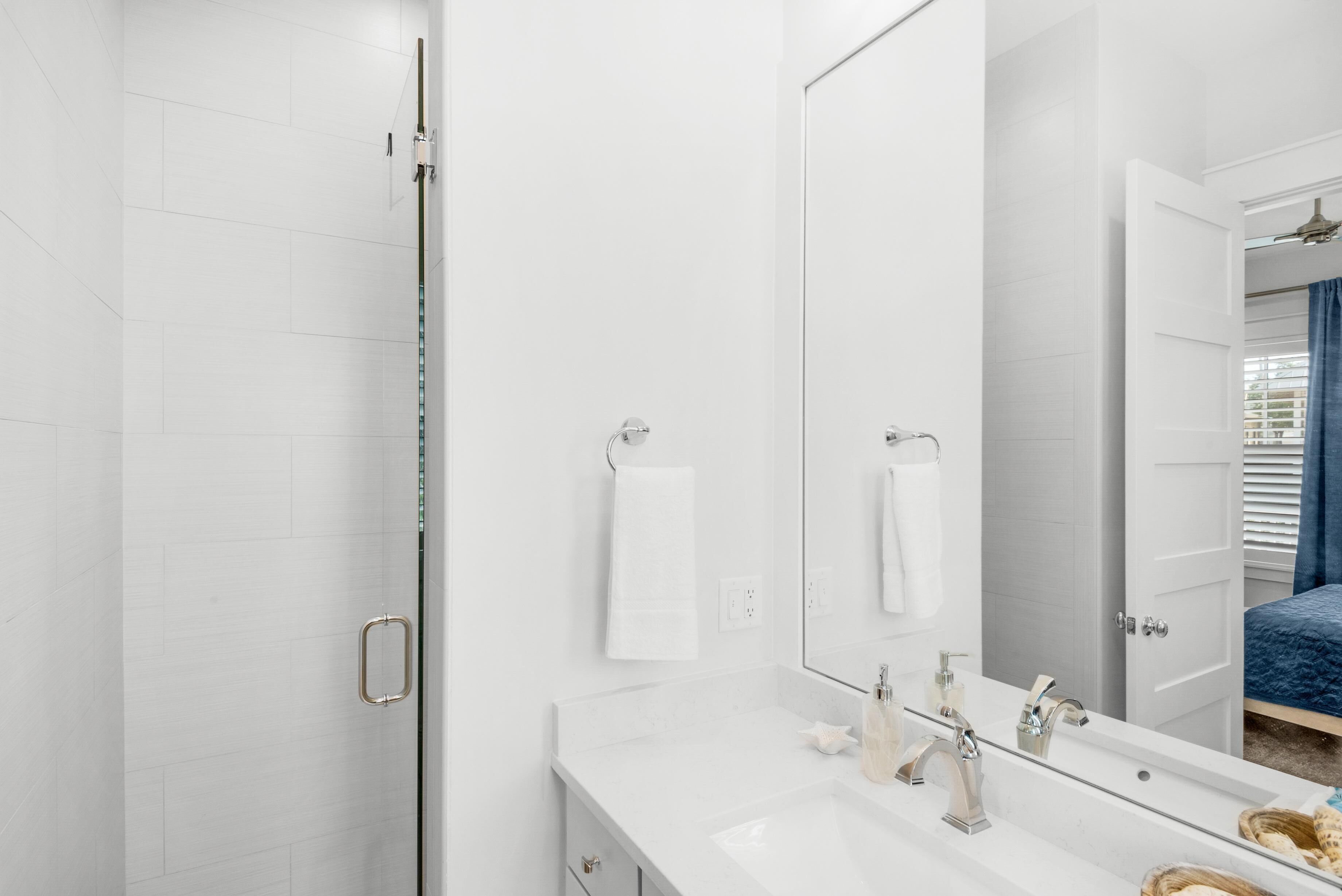 A modern bathroom with a glass shower enclosure, a large mirror, and a white countertop with a sink and vanity.