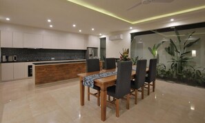 A modern kitchen with a wooden dining table and chairs, a black countertop, and a large window with plants.