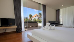 A modern hotel room with a large bed, a flat-screen TV, and a balcony with a view of palm trees and buildings. - Villa Aquila Seminyak (Seminyak)