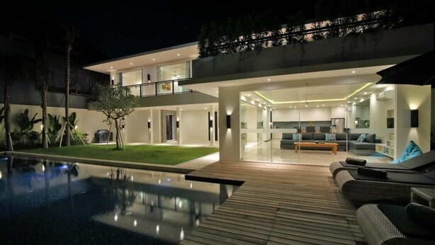 A modern house with a swimming pool, a wooden deck, and a living area with a sofa and coffee table. - Villa Aquila Seminyak (Seminyak)