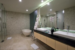 A modern bathroom with a large bathtub, two sinks, a glass shower enclosure, and a mirror with a towel rack.