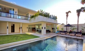 A modern two-story house with a swimming pool, outdoor seating, and a covered patio area.